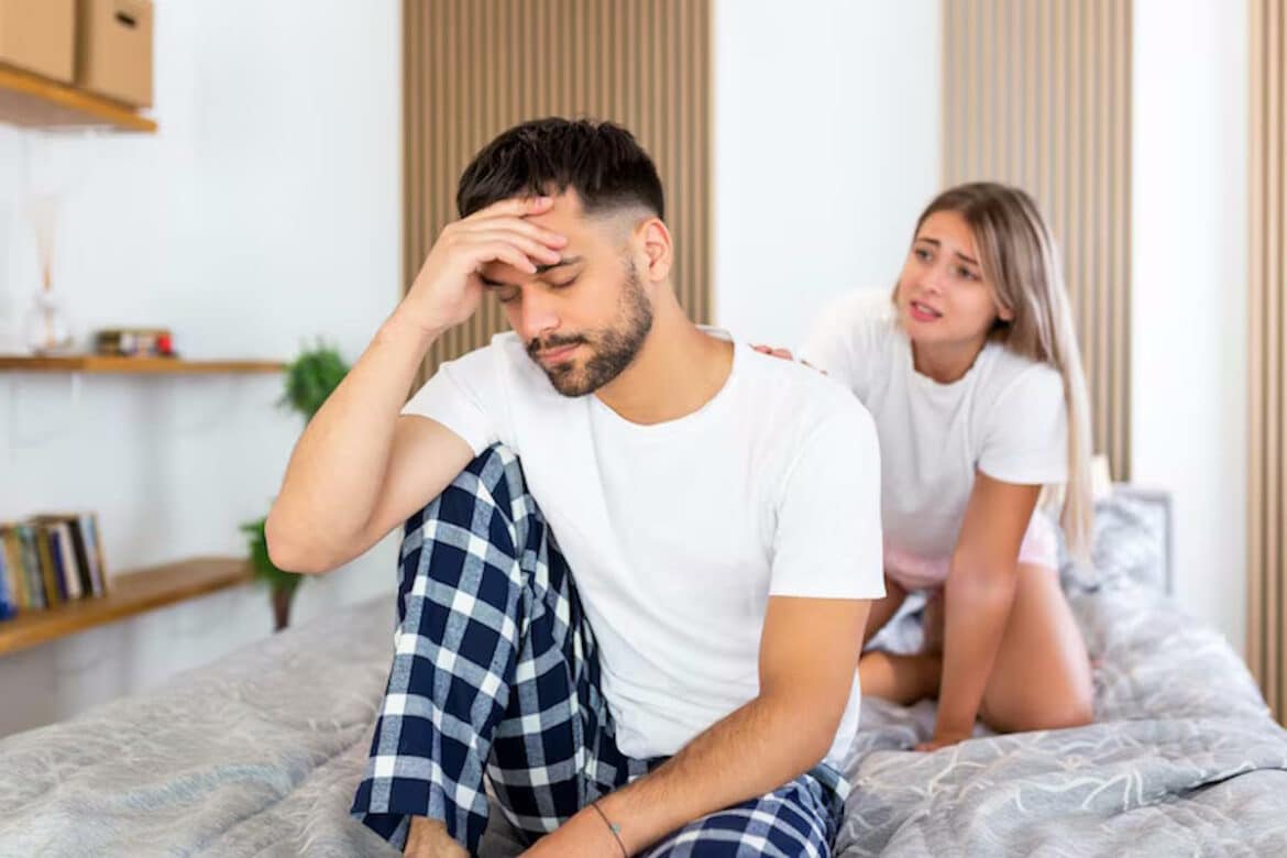 une femme qui soutient un homme assis sur le bord du lit en baissant la tête